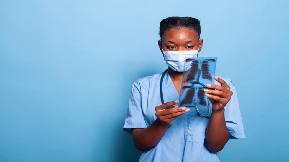 african-american-physician-assistant-with-protective-medical-face-mask-prevent-infection-with-coronavirus-analyzing-lungs-radiography-studio-with-blue-background-medicine-concept (1)