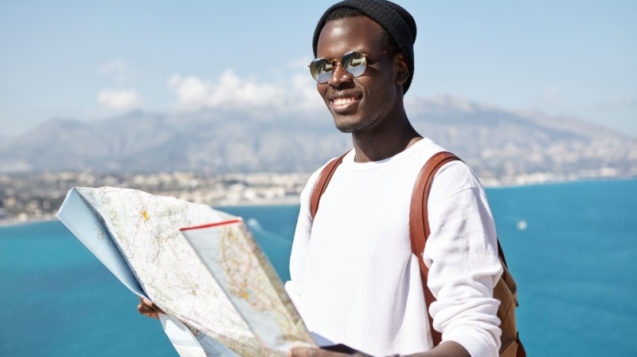 happy-handsome-young-dark-skinned-male-traveler-standing-top-mountain-with-paper-map-vast-ocean-resort-town-having-joyful-look-while-traveling-around-world-company-friends