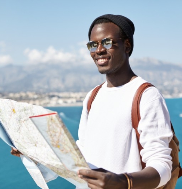 happy-handsome-young-dark-skinned-male-traveler-standing-top-mountain-with-paper-map-vast-ocean-resort-town-having-joyful-look-while-traveling-around-world-company-friends