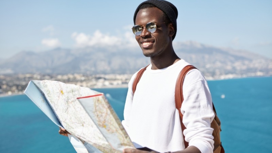 happy-handsome-young-dark-skinned-male-traveler-standing-top-mountain-with-paper-map-vast-ocean-resort-town-having-joyful-look-while-traveling-around-world-company-friends